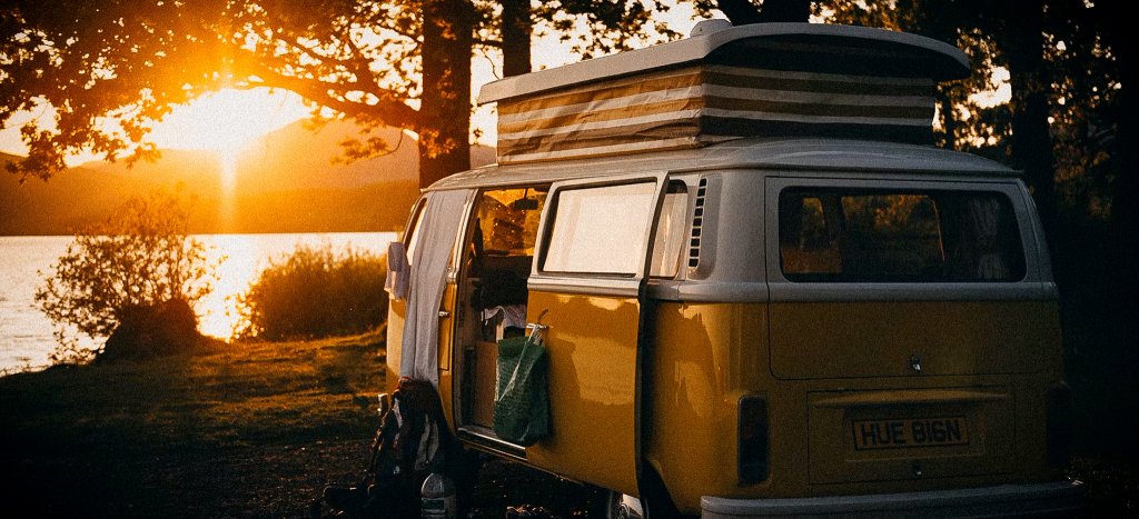 A classic yellow campervan with a pop-top roof parked by a lake at sunset, symbolizing the freedom of vanlife.